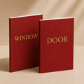 Two red hardcover books standing upright on a beige surface, one labeled "WINDOW" and the other "DOOR" in gold lettering.